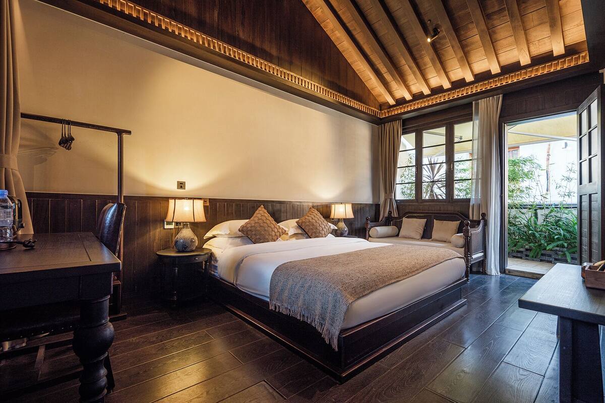 Um quarto espaçoso com uma cama grande, piso de madeira e vista para o verde pela janela.