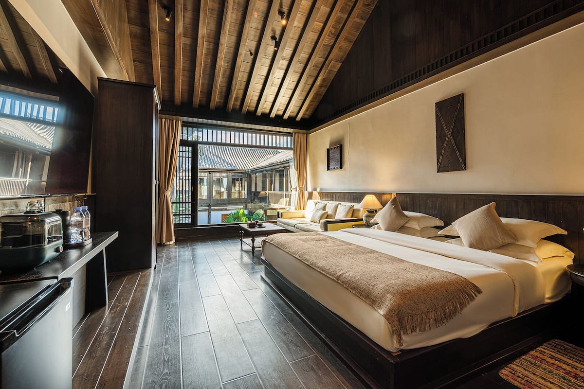 Quarto de hotel moderno com uma cama grande, uma escrivaninha com chaleira e vista para um pátio tradicional.