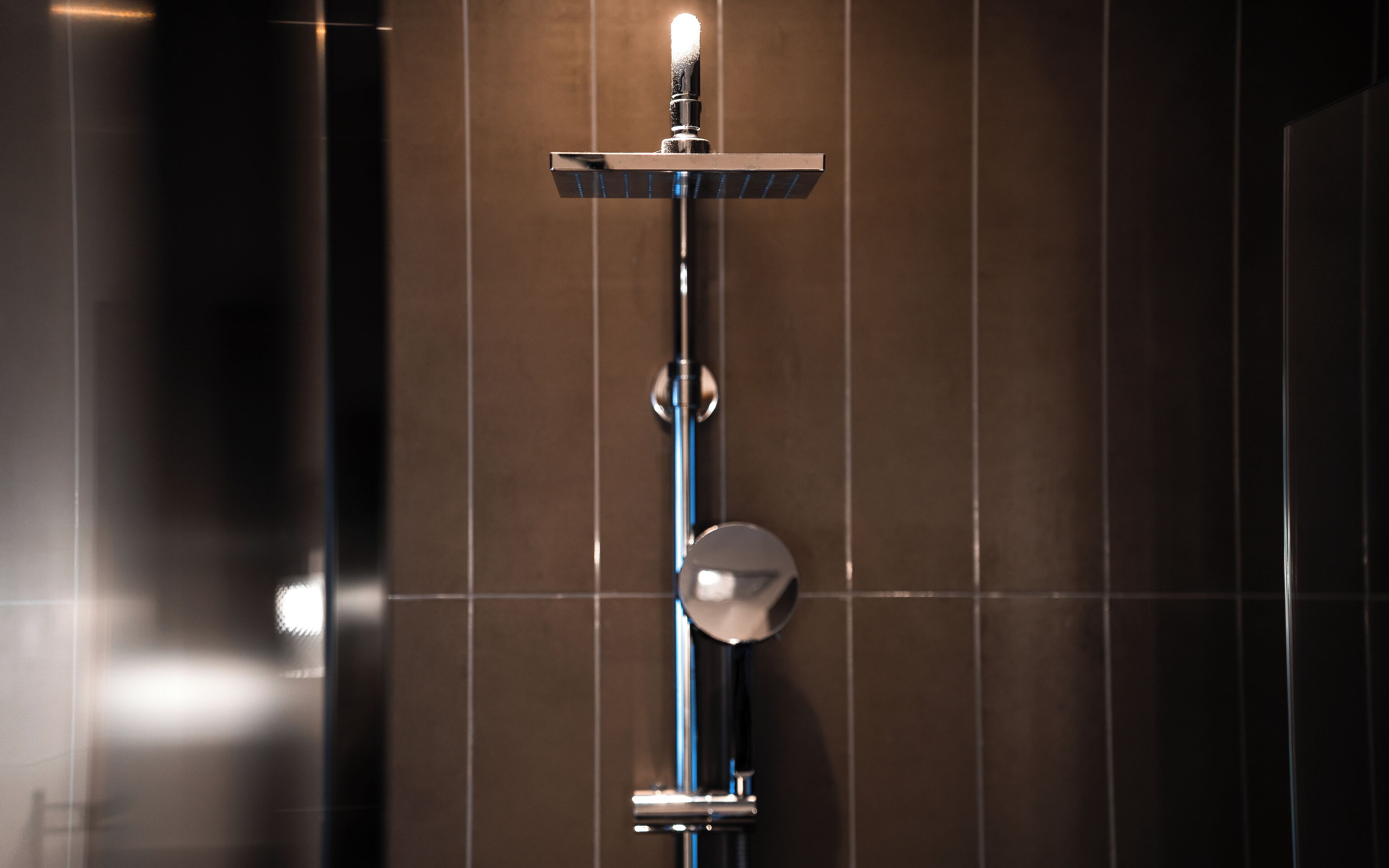 A modern shower with a vertical rain showerhead and a handheld showerhead mounted on a wall.