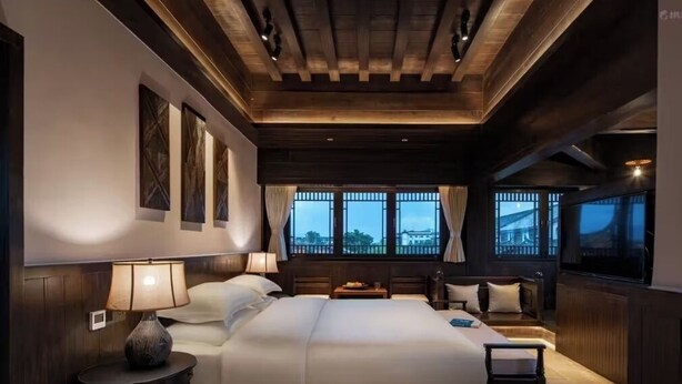 Un dormitorio amplio con una cama grande, mesitas de noche y vistas al exterior a través de amplias ventanas.