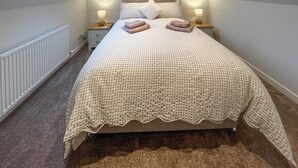 Un dormitorio con techo inclinado, un tragaluz, una cama con colcha a cuadros, dos lámparas de noche y un radiador.