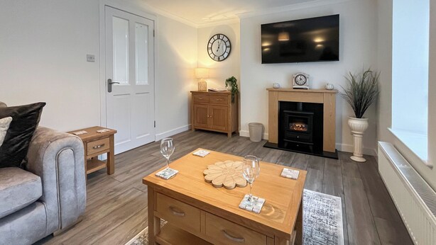 Una sala de estar moderna con un sofá, una mesa de centro de madera, chimenea, televisor y un reloj en la pared.