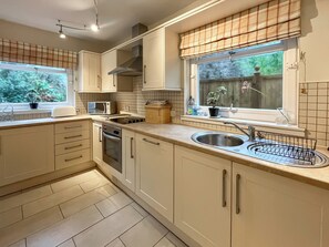 Een moderne keuken met een inbouwoven, magnetron en spoelbak, met lichtkleurige kastjes en een raam met uitzicht op groen.