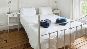 Cama bem arrumada com lençóis brancos e duas toalhas azuis, estrutura de metal branca e duas mesas de cabeceira com luminárias.