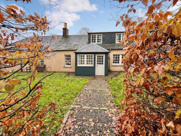 Une maison traditionnelle avec une cheminée en pierre, un chemin de gravier et une pelouse verdoyante.