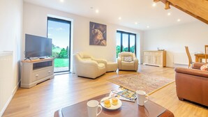 A spacious living room with a flat-screen TV, leather armchairs, a coffee table with a magazine and a mug, and a view of greenery through large windows. - Arenig View - UK51068 (Rhyd Uchaf Nr Bala)
