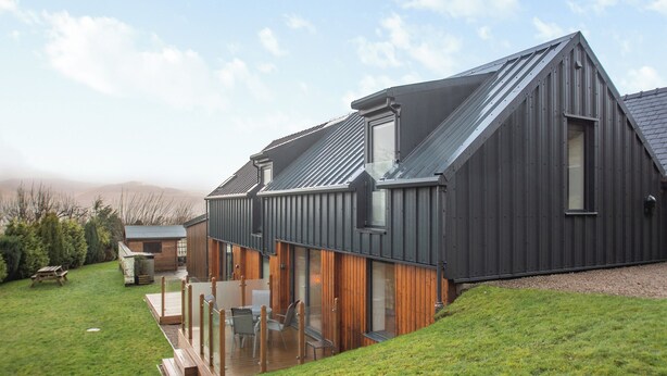 A modern house with a sloped roof, large windows, and a deck with outdoor furniture. - Arenig View - UK51068 (Rhyd Uchaf Nr Bala)