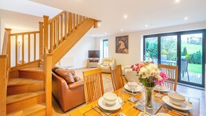 A spacious living area with a wooden staircase, a leather sofa, a dining table set for four, and a large window offering a view of the outdoors. - Arenig View - UK51068 (Rhyd Uchaf Nr Bala)