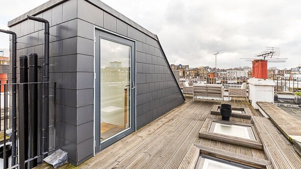 En takterrass med en modern, mörkfärgad konstruktion, en glasdörr och utsikt över stadsbilden.