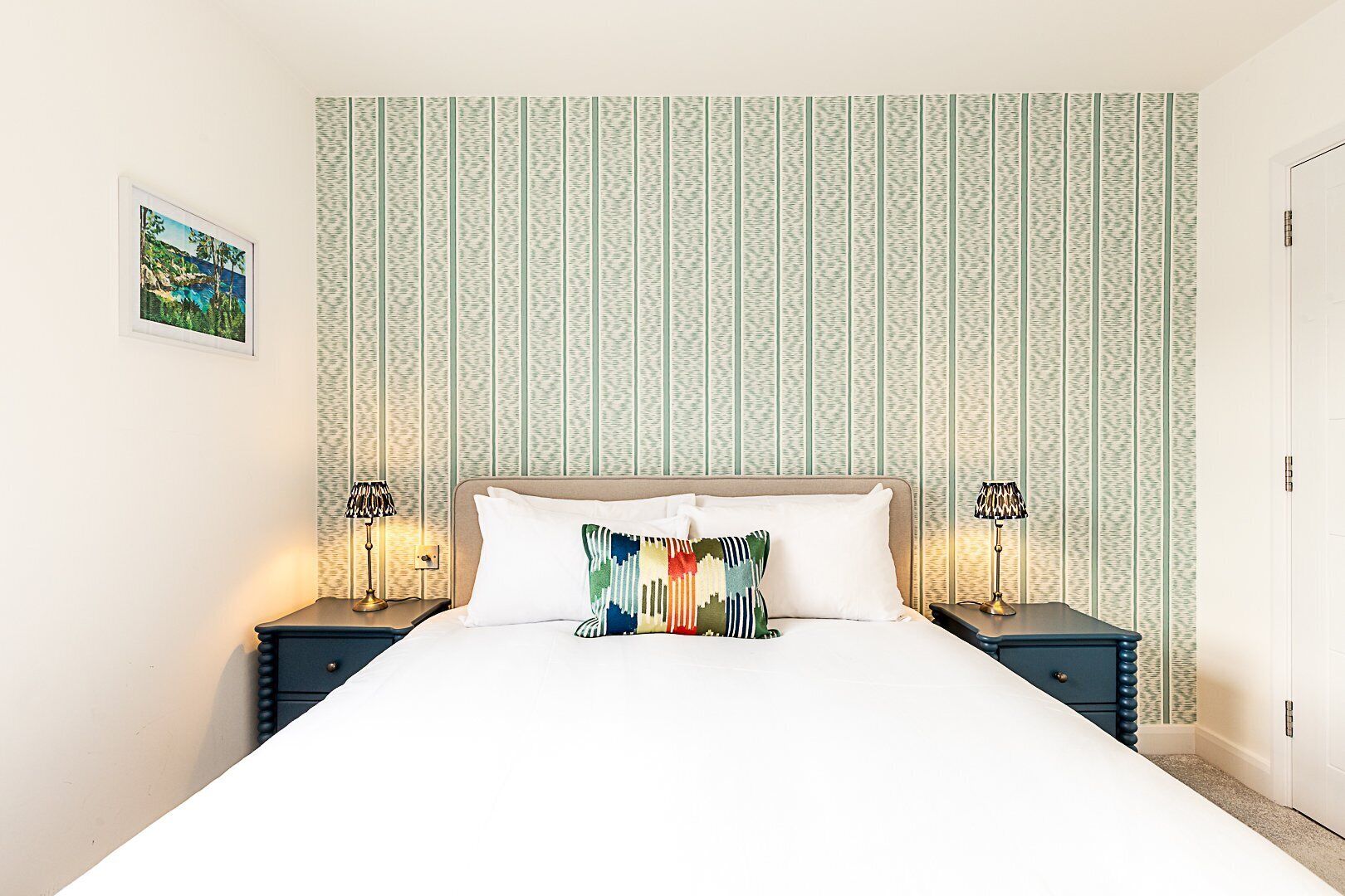 A neatly made bed with a colorful pillow, two bedside tables with lamps, and a patterned wallpaper.