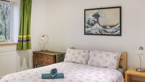 A bedroom with a bed, a nightstand, a dresser, a window with curtains, and a wall-mounted painting. - Spacious house sleeping ten, perfect for large families or groups. (Pembroke)