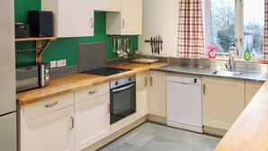 A kitchen with white cabinets, a wooden countertop, a Bosch dishwasher, and a window with checkered curtains. - Spacious house sleeping ten, perfect for large families or groups. (Pembroke)