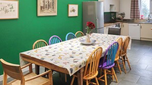 A dining area with a green wall, a wooden table, colorful chairs, and framed artwork. - Spacious house sleeping ten, perfect for large families or groups. (Pembroke)