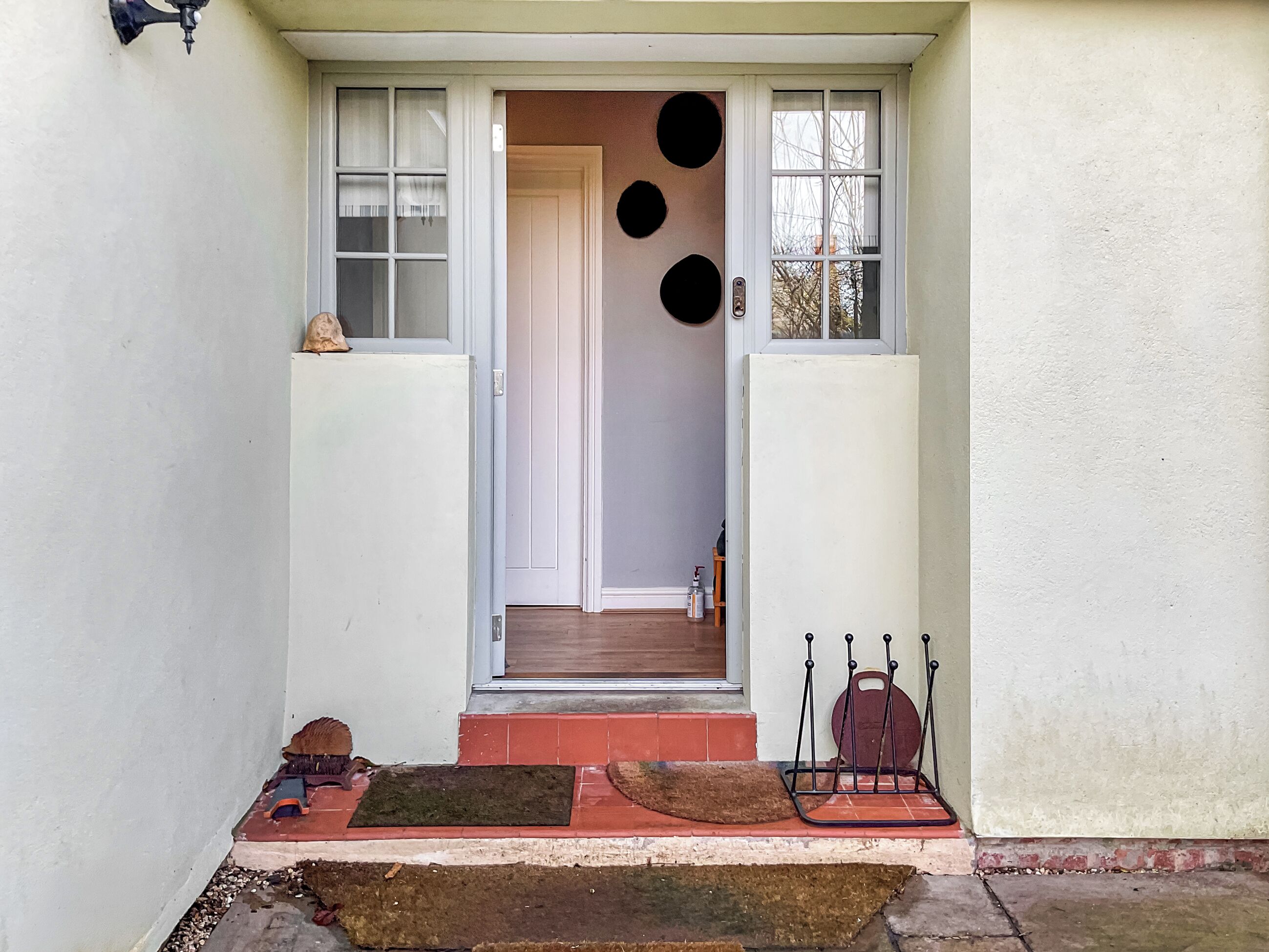 A house entrance with a white door, a small porch with a red mat, and a metal chair.