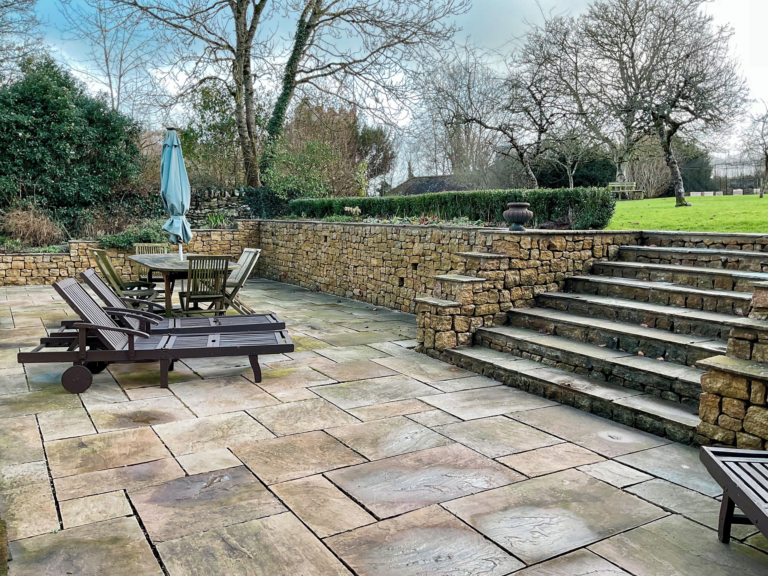 A patio with stone steps, a table with chairs, and a blue umbrella.