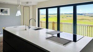 Een moderne keuken met een groot eiland, een inbouwspoelbak en uitzicht op een groen landschap door grote ramen.