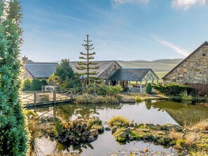 Ein rustikales Steinhaus mit einer Holzterrasse und einem Teich davor.