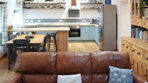 A modern kitchen with a central island, wooden cabinets, and a dining area with a leather sofa. - Stable Cottage - UK51203 (Fishguard)