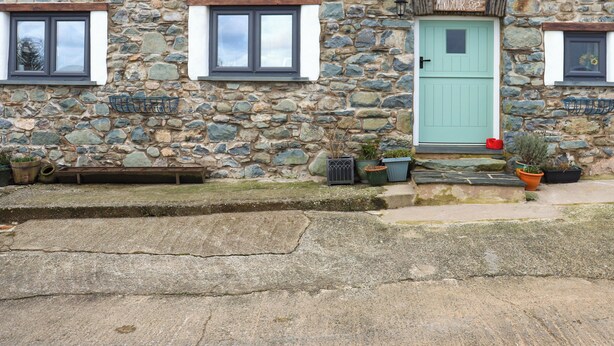 A stone house with a green door, two windows, and a small porch with potted plants. - Stable Cottage - UK51203 (Fishguard)