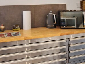 A kitchen counter with a paper towel holder, a kettle, and a microwave. - Maids Cottage - UK51204 (Fishguard)