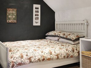 Ein Schlafzimmer mit einem Bett, einem Nachttisch, einem an der Wand befestigten Regal, einem gerahmten Foto und einem Schild an der Wand.