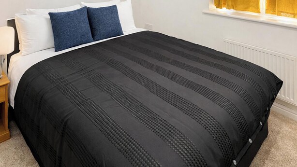 A neatly made bed with a black and grey striped duvet, white pillows, and a wooden nightstand with a lamp. - 2 bedroom accommodation in Westwood, near Margate (Westwood, near Margate)