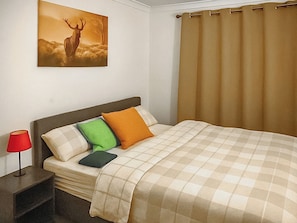 Ein Hotelzimmer mit einem Bett, einem Nachttisch, einer Lampe, einem Bild eines Rehs und einem Fenster mit Vorhängen.