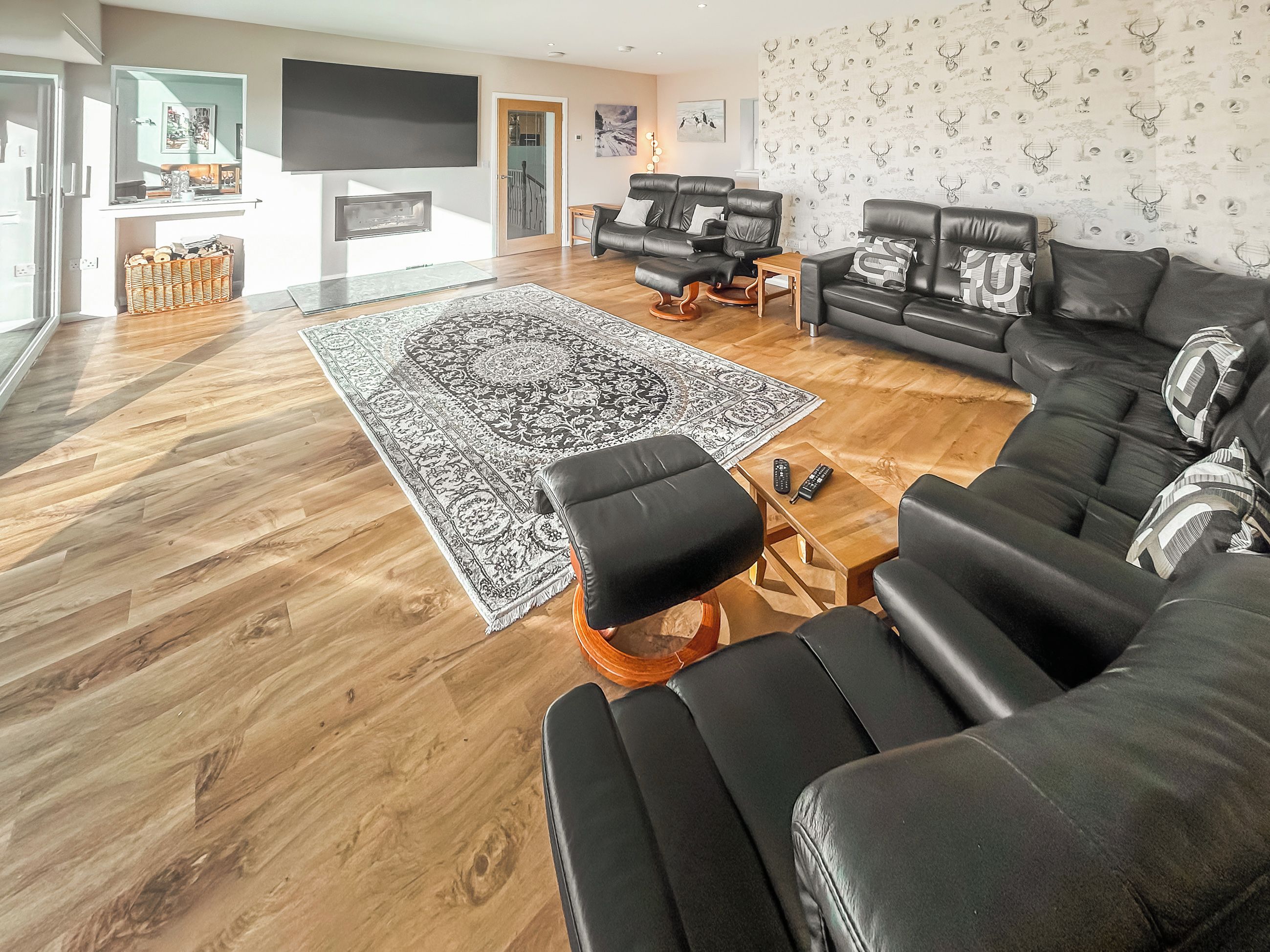 Un salon moderne avec un grand canapé en cuir noir, un tapis à motifs et une table basse en bois.