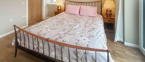 Un dormitorio con estructura de cama de madera, ropa de cama floral, una ventana y dos lámparas de noche.