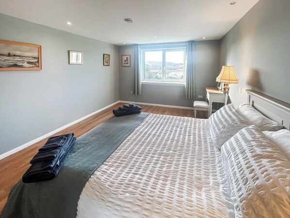 A hotel room with a bed, a desk, a chair, a window with curtains, and a lamp.