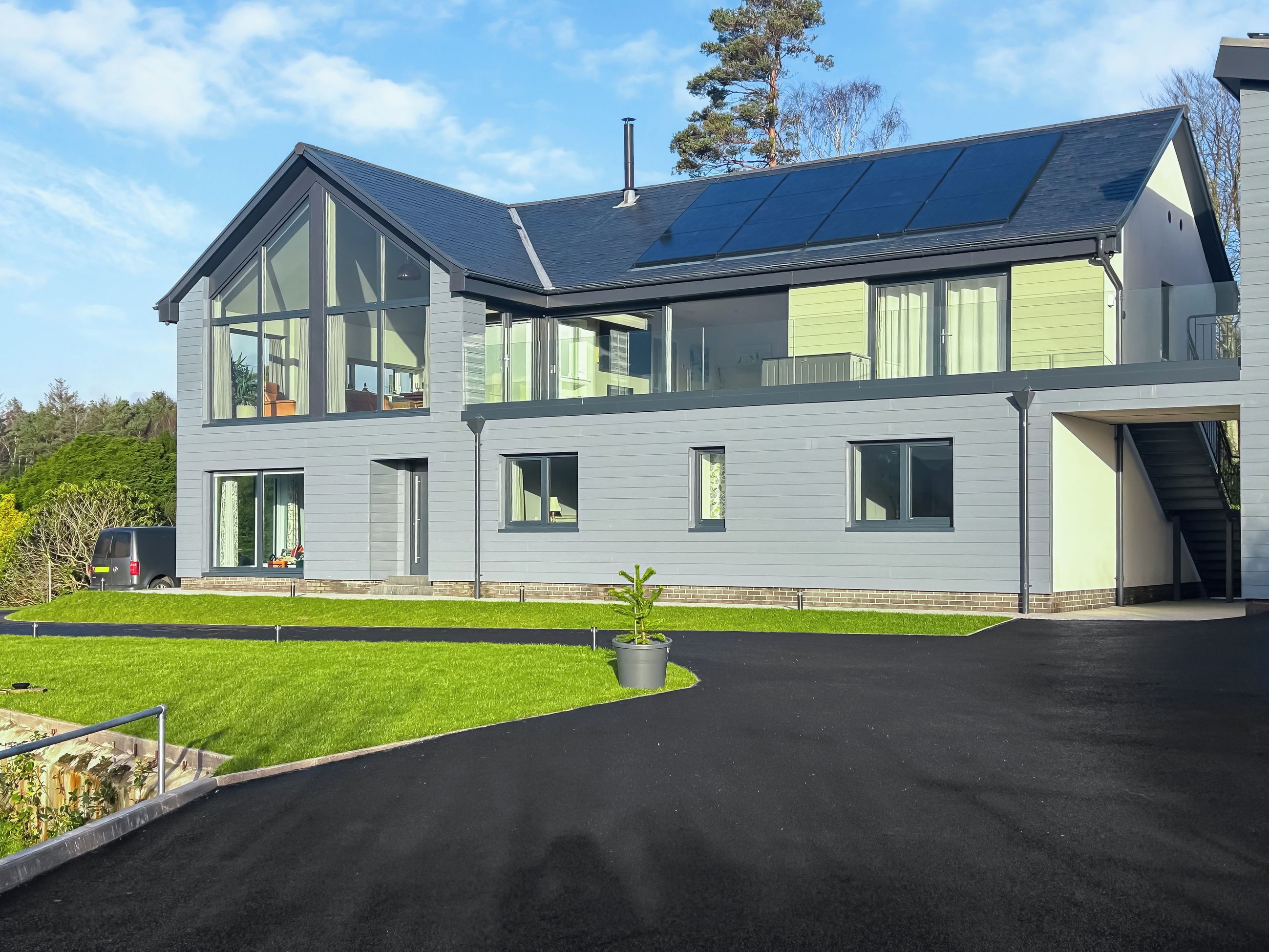 Et moderne hus med to etager, store vinduer, solpaneler på taget og en velholdt græsplæne.