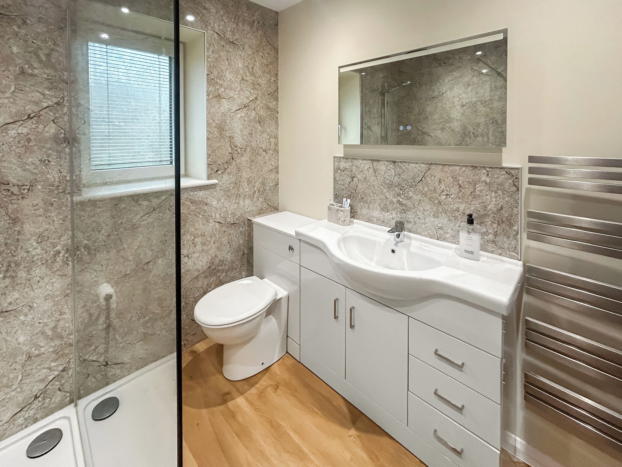 Un baño moderno con pared de mármol, inodoro, lavabo con espejo y zona de ducha.