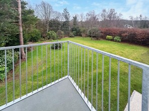 A balcony with a metal railing overlooking a well-maintained lawn and trees.
