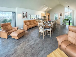 Een ruime woonkamer met leren banken, een eettafel gedekt voor zes personen en een keuken op de achtergrond.