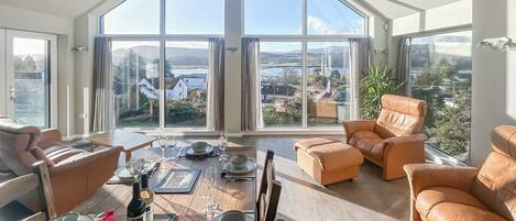 Een ruime woonkamer met een hoge plafond, grote ramen en uitzicht op het omliggende landschap.