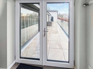 A glass door leading to a balcony with a tiled floor and a view of a building and trees.