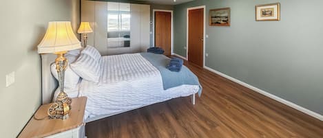 Een slaapkamer met een bed, twee bedlampen, een houten nachtkastje, een kledingkast en een deur naar een andere kamer.