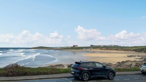 A coastal road with a parked SUV, a sandy beach, and a clear sky. - 1 bedroom accommodation in Newquay (Newquay)