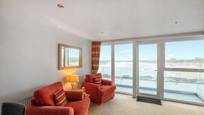 A room with two red sofas, a lamp, a mirror, and large windows with a view of the beach. - 1 bedroom accommodation in Newquay (Newquay)