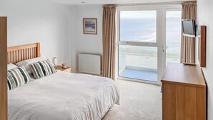 A bedroom with a bed, a nightstand, a TV, and a view of the sea through a large window. - 1 bedroom accommodation in Newquay (Newquay)