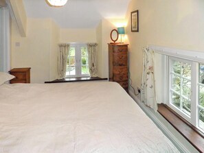 Ein Schlafzimmer mit einem großen Bett, einem Schminktisch, einem Spiegel und einem Fenster mit Vorhängen.