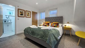 Ein Schlafzimmer mit Bett, Nachttisch, Lampe und Blick ins Bad.