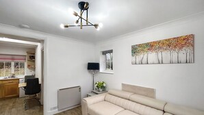 Ein modernes Wohnzimmer mit einem beigen Sofa, einem Essbereich mit Tisch und Stühlen, einem Heizkörper und einem Fenster mit Blick auf Bäume.