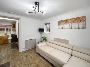 Un salón moderno con un sofá color beige, una zona de comedor con mesa y sillas, un radiador y una ventana con vistas a árboles.