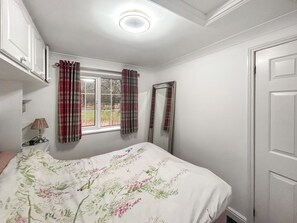 Ein Schlafzimmer mit Bett, Vorhängen am Fenster, einem Spiegel und einer Tür.