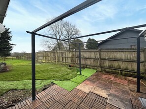 Un patio trasero con una terraza de madera, un pérgola de metal y un área cercada.