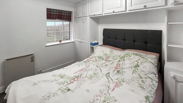 Ein Schlafzimmer mit Bett, Fenster mit Jalousien, Heizkörper und Einbauschränken.