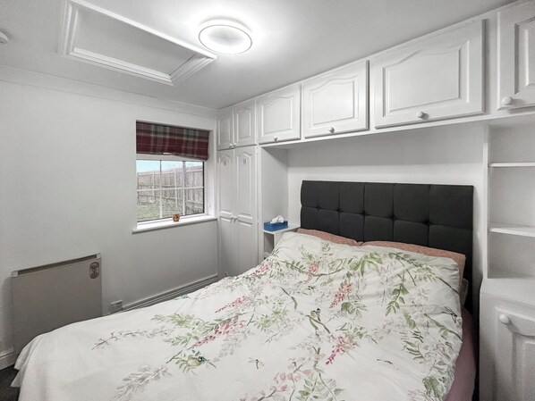 A bedroom with a bed, a window with blinds, a radiator, and built-in shelving.