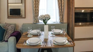 A dining area with a wooden table set for four, a vase with flowers, and a modern kitchen in the background. - 2 bedroom accommodation in Wisemans Bridge (Wisemans Bridge)