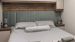 A neatly made bed with pillows, a wooden headboard, bedside lamps, and folded towels on the nightstand. - 2 bedroom accommodation in Wisemans Bridge (Wisemans Bridge)